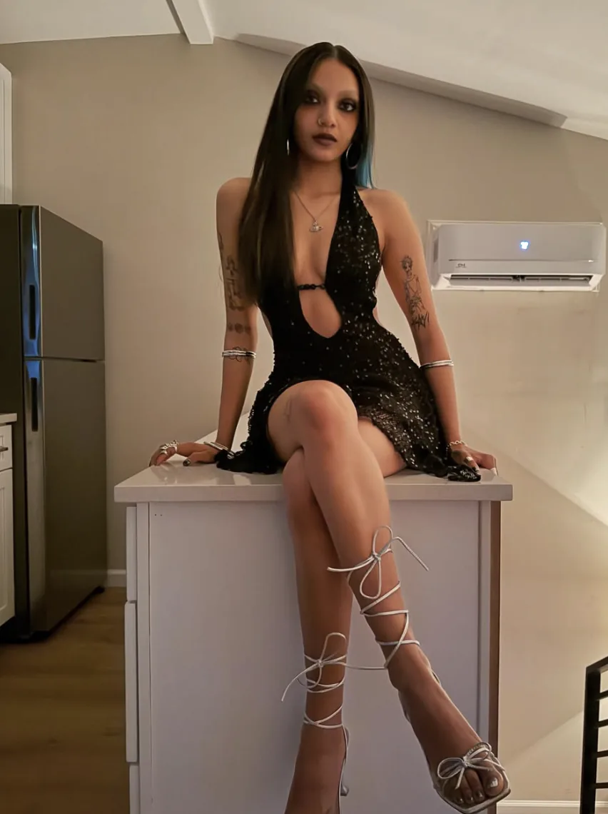 K⭐Y seated on a counter in a black dress and laced heels